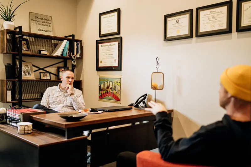 A therapist at his desk, listening to a man seated across from him, in an office at Reclaim Recovery